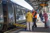 Staff assisting passenger with mobility aid onto train with ramp deployed at a station